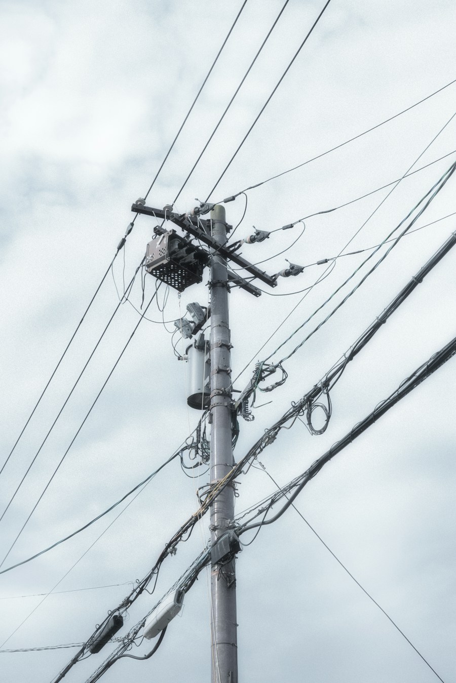 Power lines crossing a pole against a cloudy sky