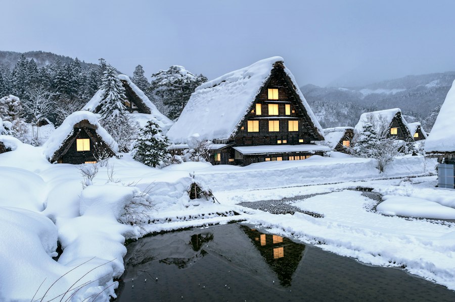 Snowed-in village with lit windows at dusk
