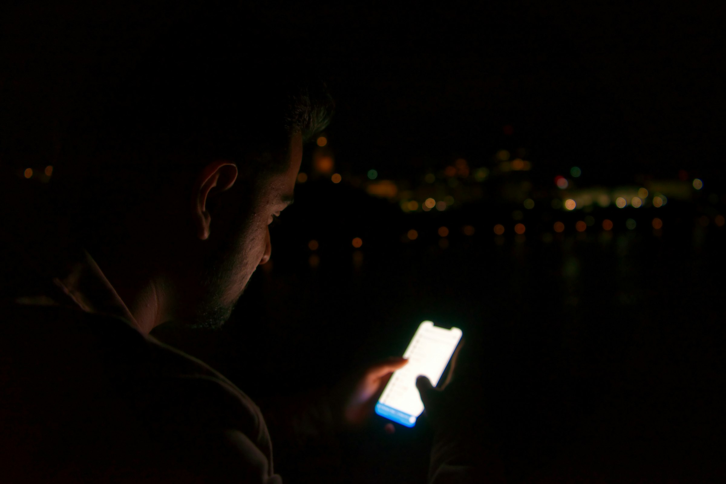 A man in the dark lit only by the glow of his phone