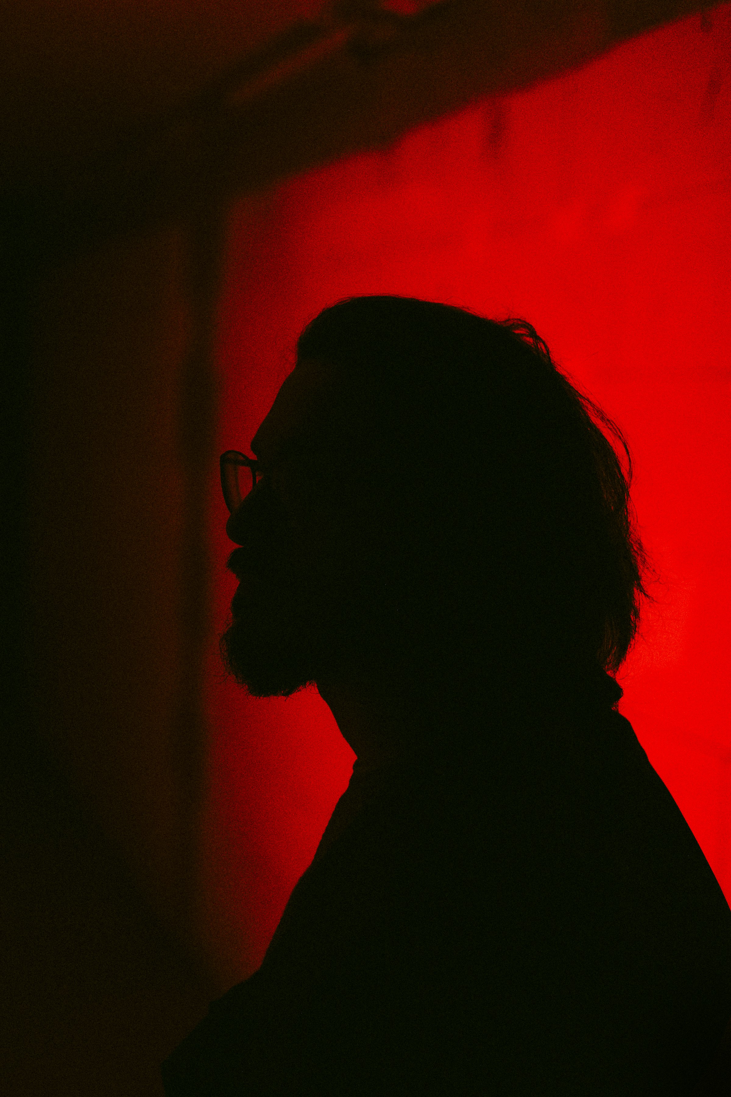 Silhouette of a man with glasses against a red wall