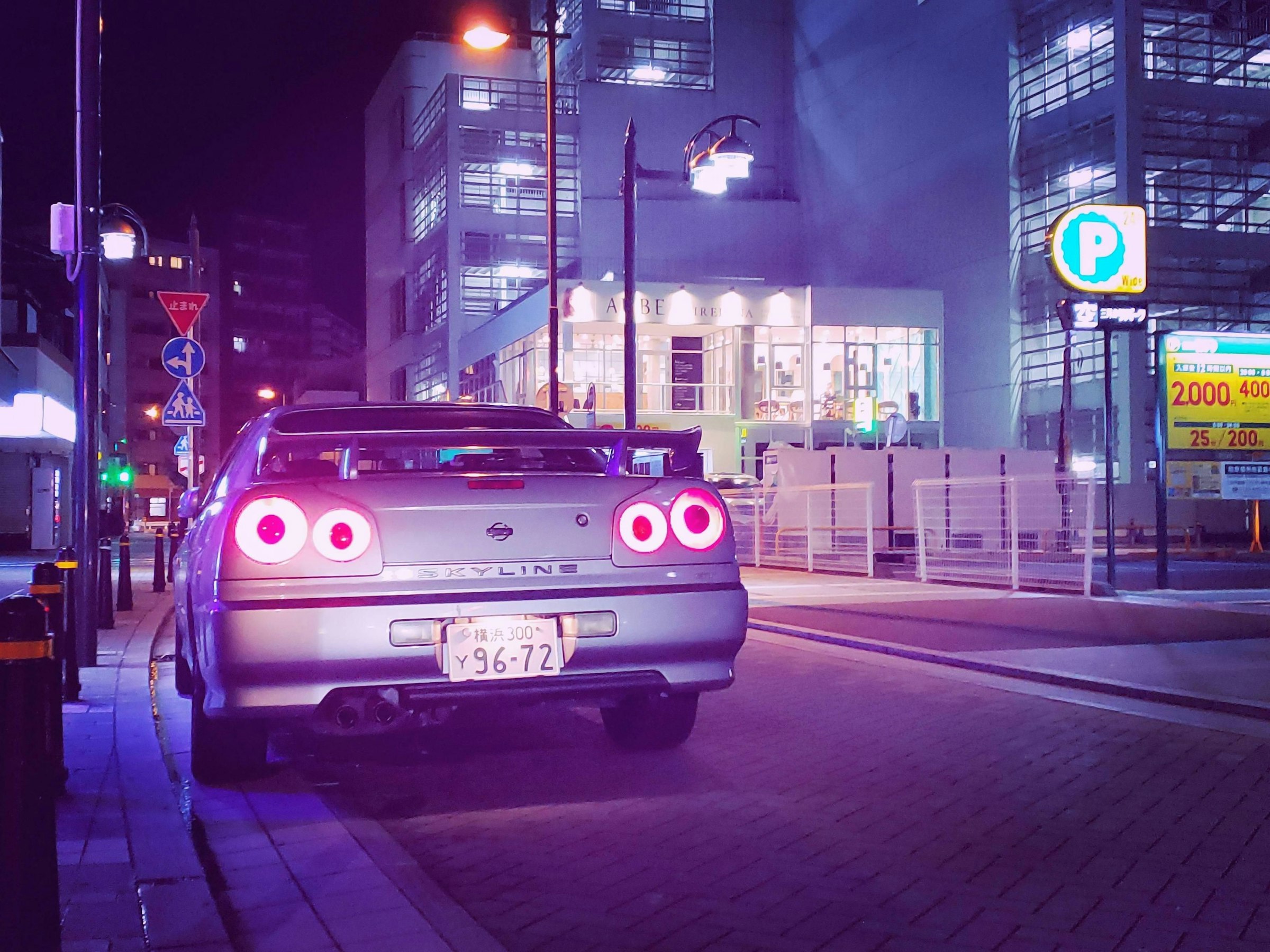 A silver sports car parked on a neon-lit street at night